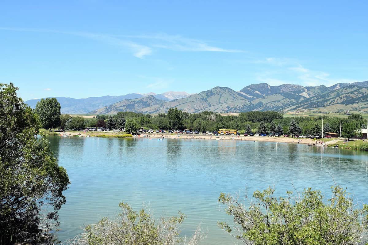 A scenic view from MAP Brewing's patio of a lake surrounded by trees and mountains under a clear blue sky. 