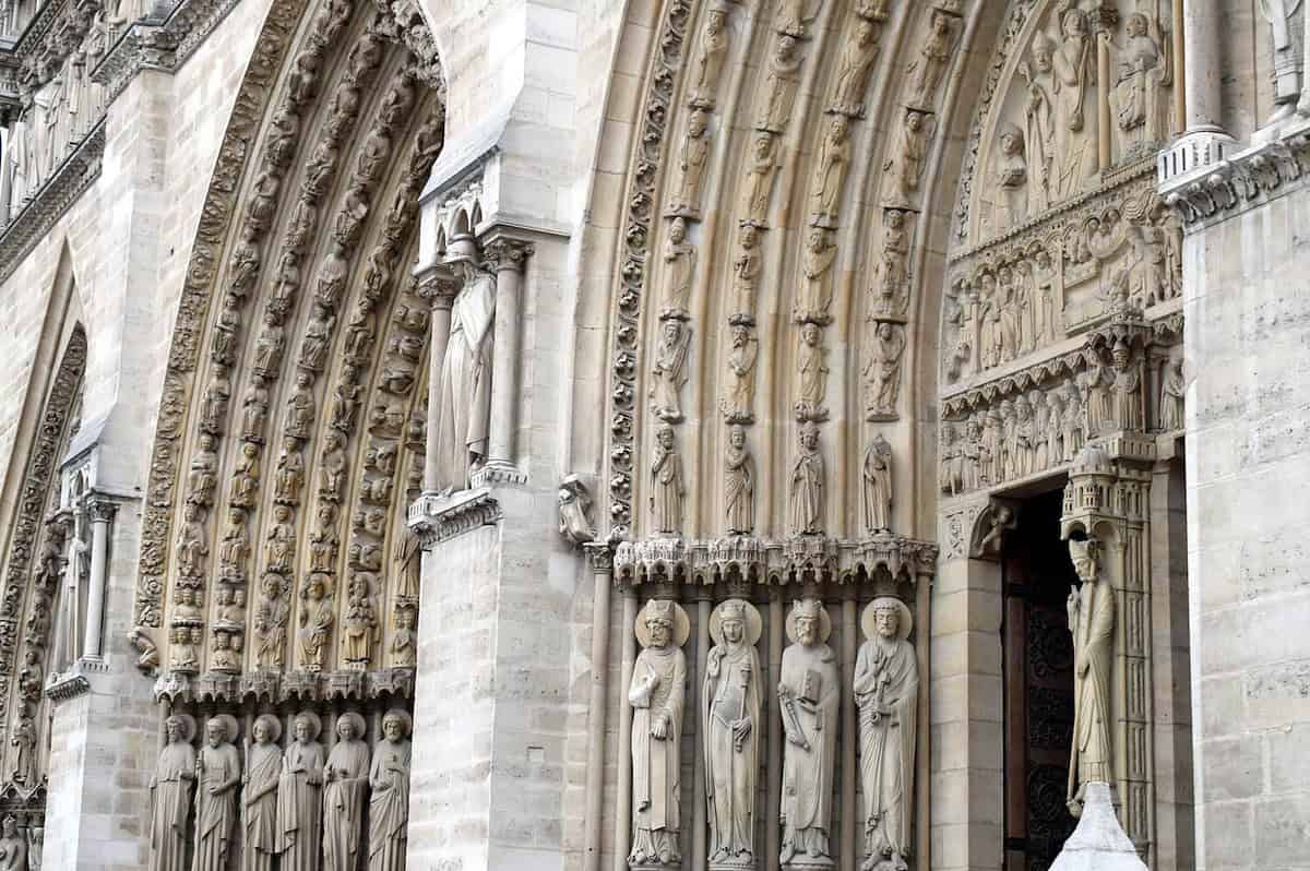 A close-up of Notre-Dame Cathedral's ornate facade in Paris showcases detailed stone carvings of religious figures and intricate Gothic elements, including columns, arches, and statues. It's a captivating sight for parents exploring Paris with kids.