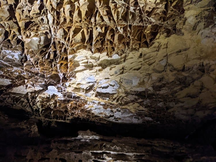 During a spring break in Amsterdam, you might encounter a cave ceiling featuring intricate formations with jagged, angular rock patterns. The surface is illuminated, highlighting the textures and earthy tones of the stone.