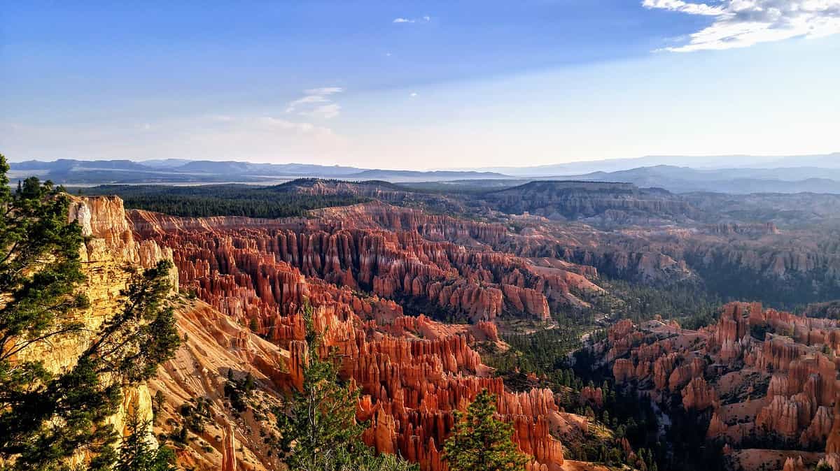 A picturesque view of Bryce Canyon with stunning red rock formations under a clear blue sky. The unique hoodoos, reminiscent of biking the Swamp Rabbit Trail with kids through diverse landscapes, create a striking contrast against the green foliage and distant mountain ranges.
