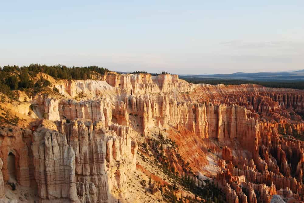 A breathtaking view of Bryce Canyon National Park at sunrise. The image showcases orange and red hoodoos and a forested horizon under a clear sky.