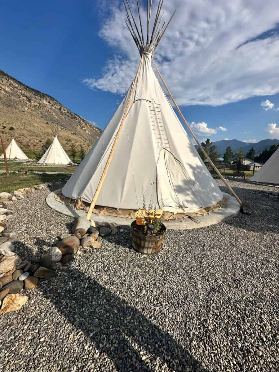 A large white tipi on a gravel ground with mountains in the background.